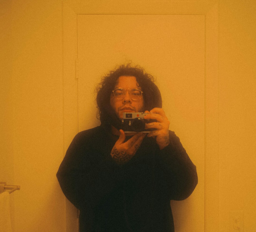 Studio portrait of a young man with curly dark hair holding a camera