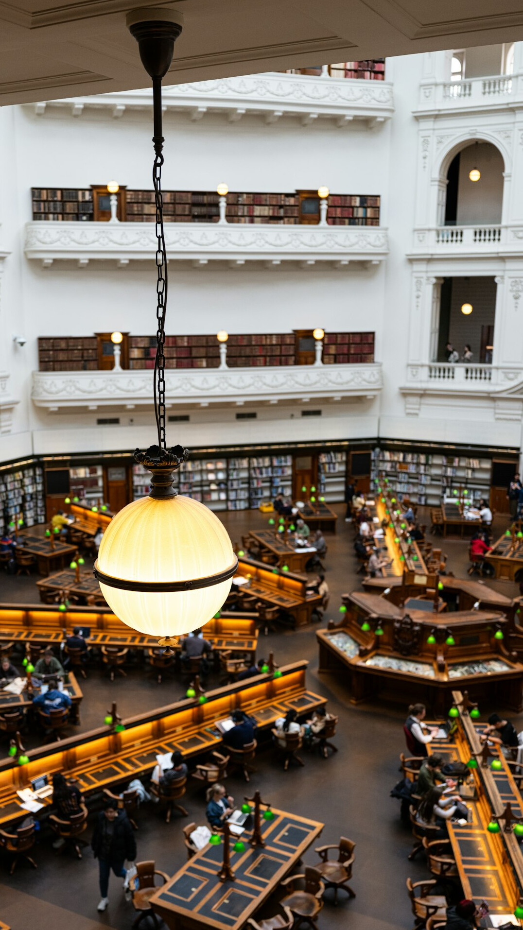 Historic library reading room with tall wooden shelves and green lamps